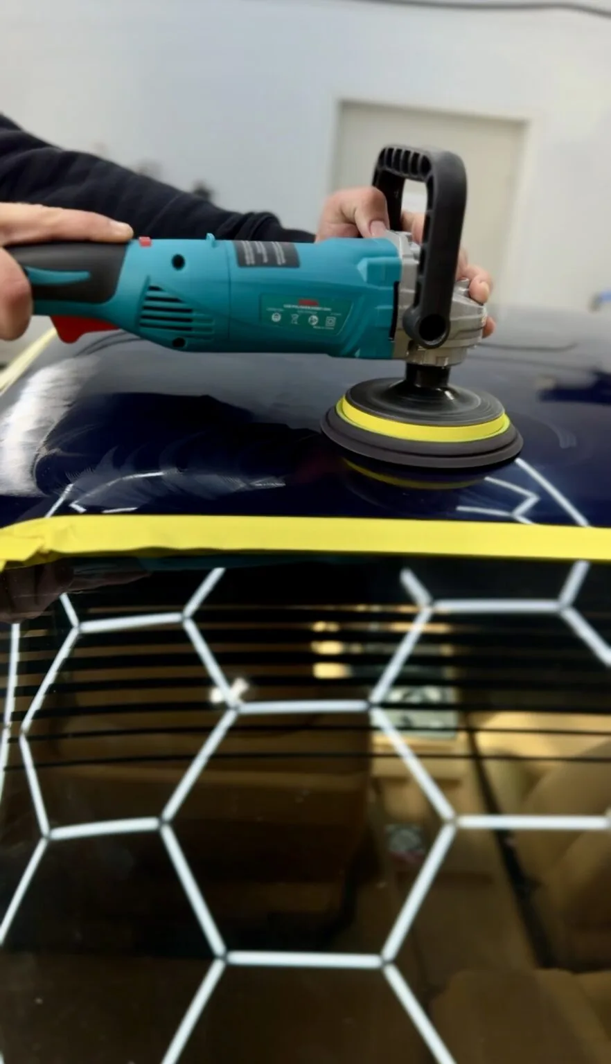 Close-up of a professional car detailer using a power polisher on a vehicle’s surface to achieve a high-gloss finish