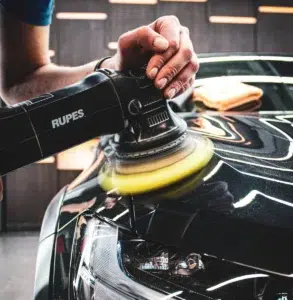 Detailing specialist using a Rupes polisher on a car’s hood for a high-gloss finish.