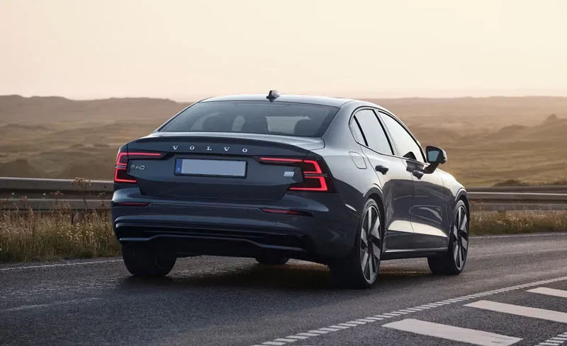 Rear view of a Volvo S60 sedan driving on an open road at sunset, showcasing its modern LED taillights and sleek Scandinavian design.