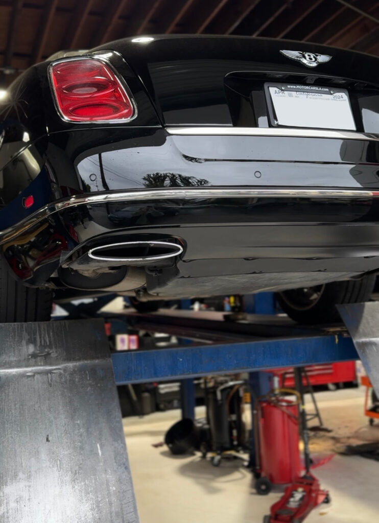 Rear view of a black Bentley on a lift with visible exhaust system during inspection at European Auto Service in Reseda, Los Angeles