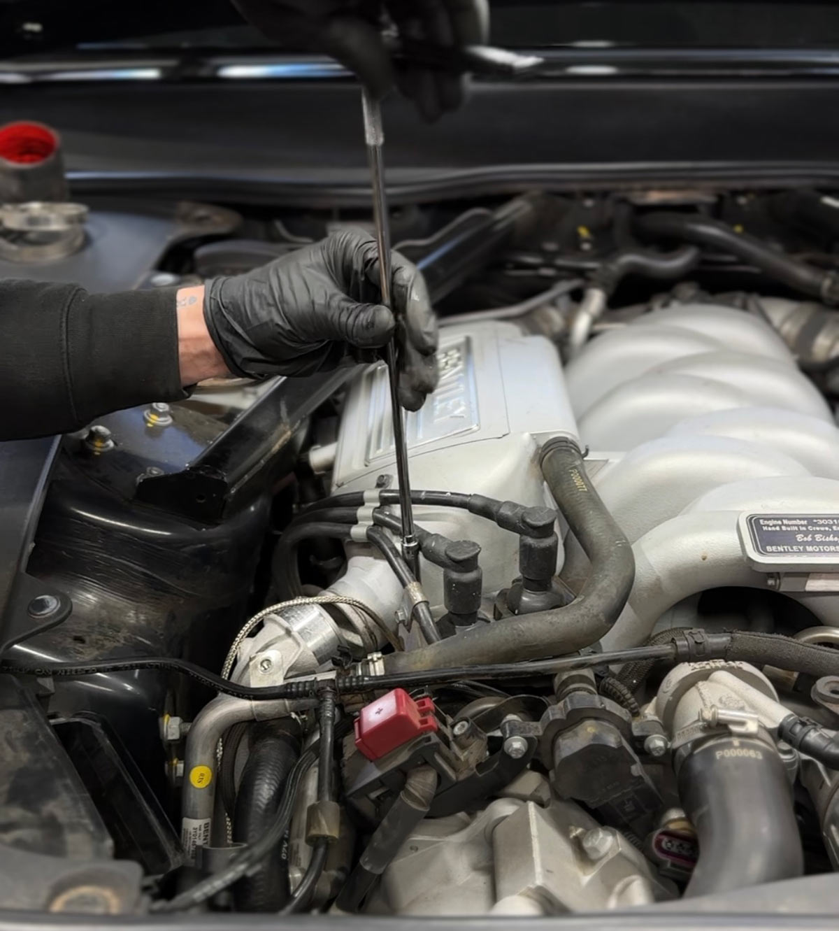 Technician performing engine diagnostics on a Bentley with Hand Built in Crewe engine plaque visible in the bay