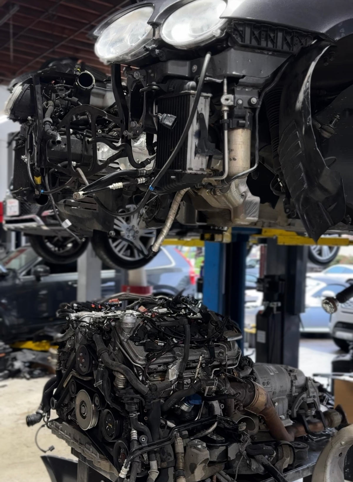 Bentley Continental engine and transmission assembly removed and placed below the lifted vehicle during major drivetrain repair