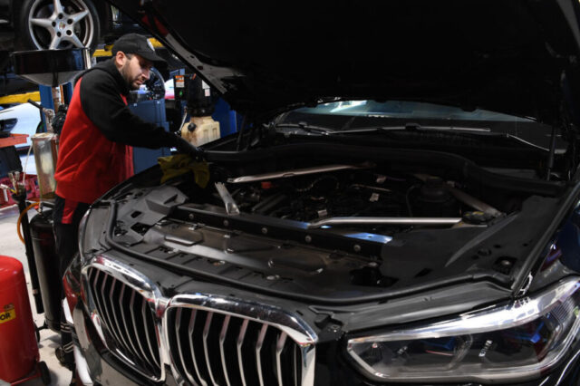 European Auto Service technician performing engine maintenance on BMW X7 with hood open in Los Angeles shop