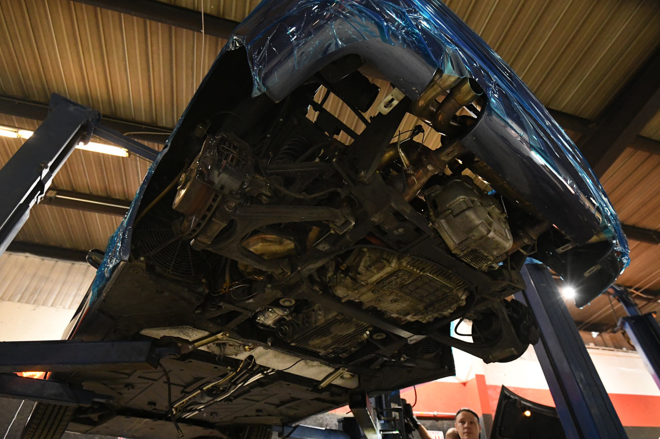 Ferrari raised on lift with protective blue film showing exposed aluminum undercarriage and drivetrain components during specialist inspection