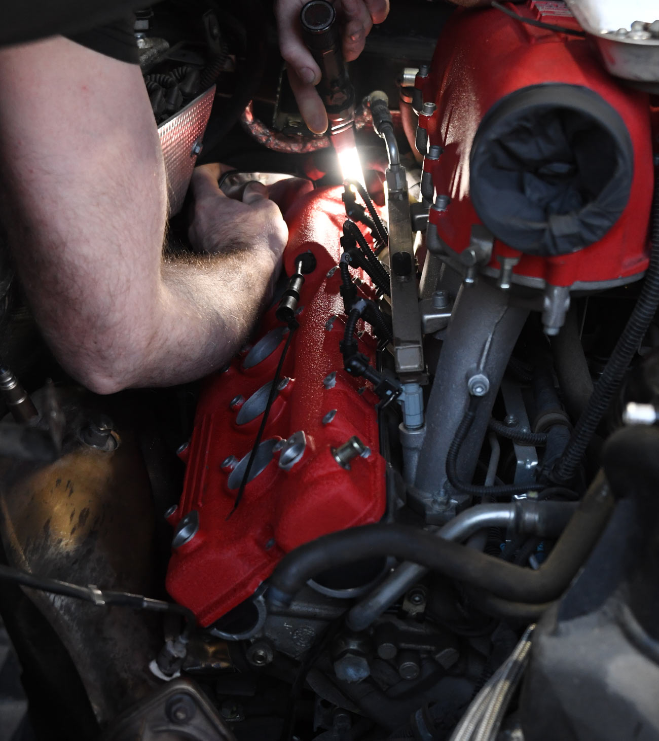 Close-up of technician hands working on Ferrari V8 engine with red valve covers and ignition coil wiring during precision service