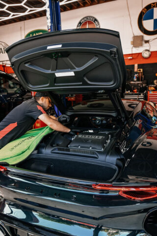 lotus-emira-engine-repair-specialist-los-angeles European Auto Service technician performing Lotus Emira V6 engine maintenance in Los Angeles shop, with BMW and Mercedes logos visible on wall