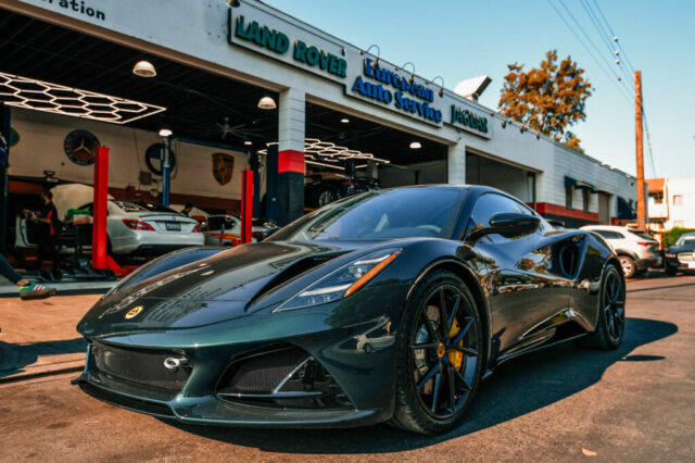 lotus-emira-repair-european-auto-service-los-angeles Dark green Lotus Emira parked outside European Auto Service repair shop in Reseda, Los Angeles, with service bay and red lifts visible in the background
