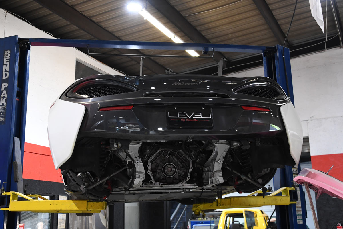 McLaren 570GT elevated on lift with rear bumper removed showing exposed drivetrain and engine bay during specialist service