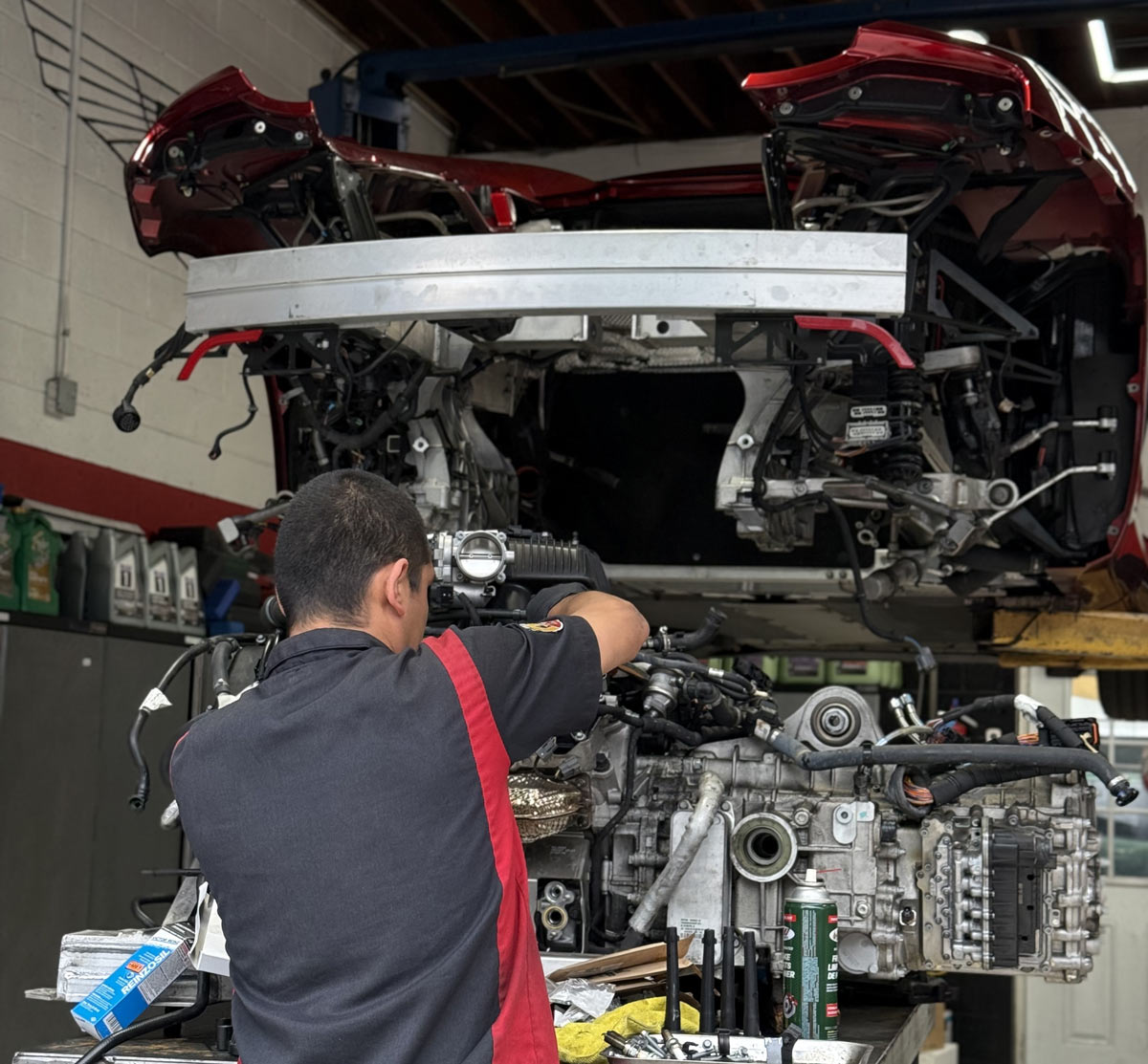 Technician working on removed McLaren twin-turbo engine on stand with red McLaren elevated on lift in background at European Auto Service