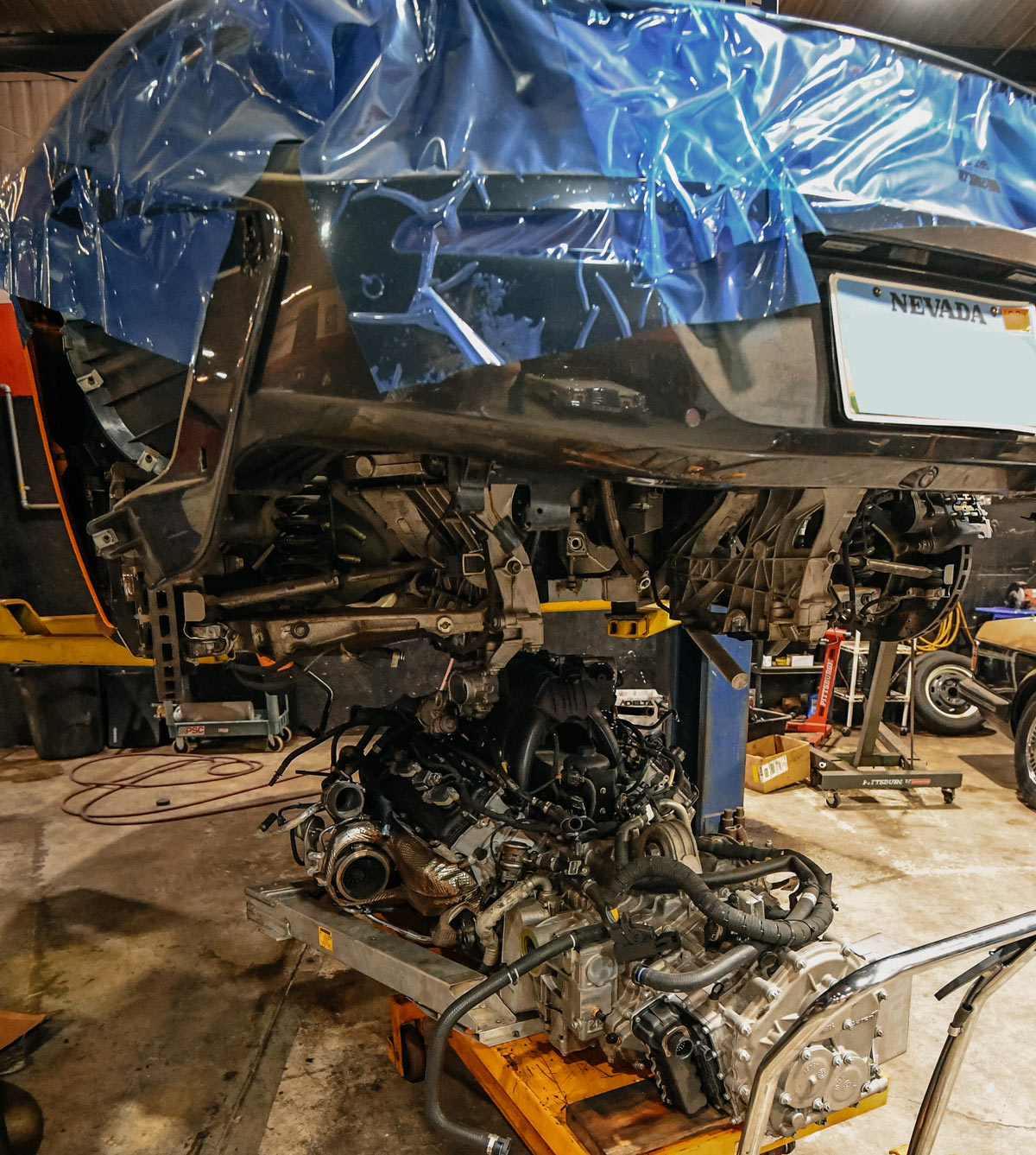McLaren with engine and transmission removed on hydraulic jack showing carbon fiber monocoque structure with protective blue wrap during major overhaul