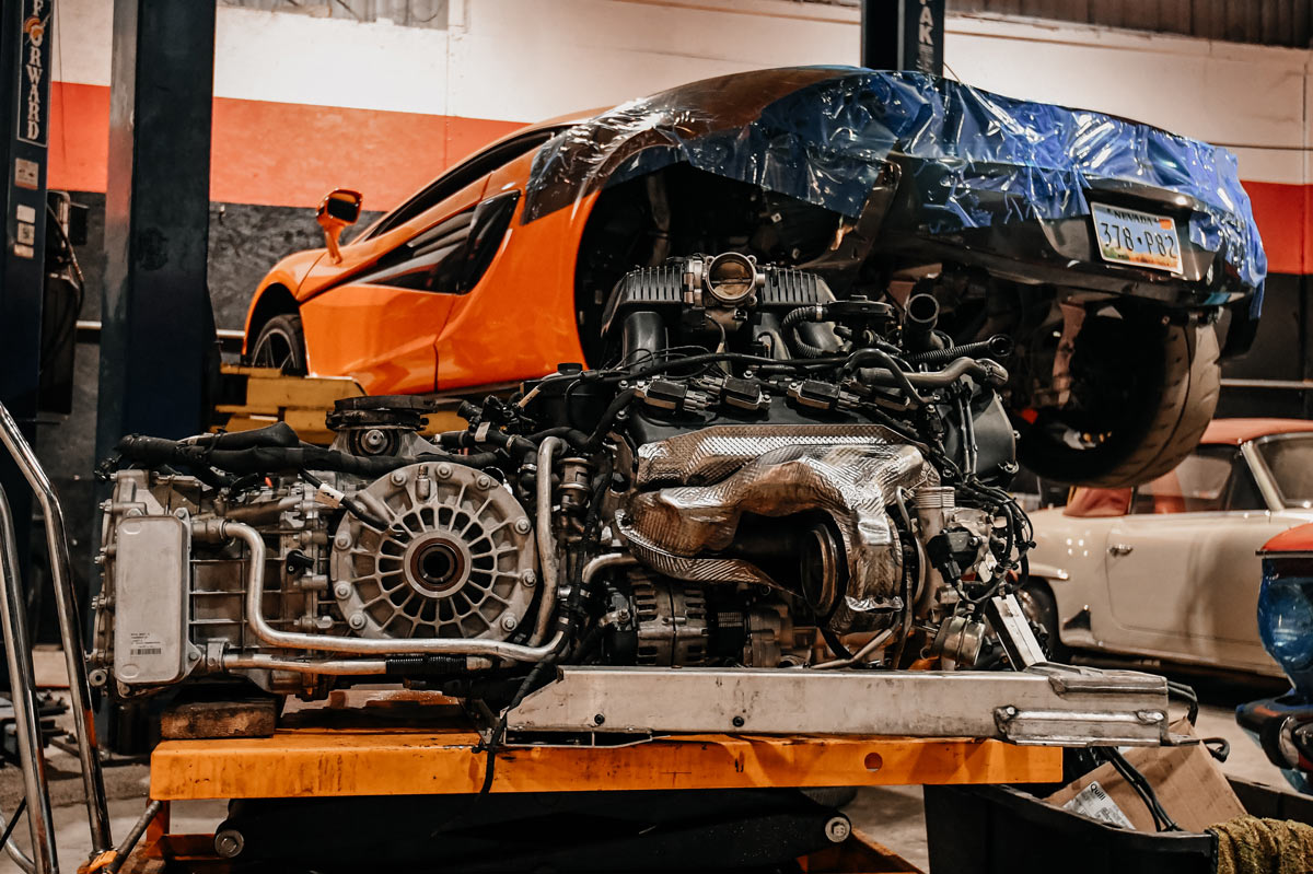 McLaren twin-turbo V8 engine and transmission assembly on engine stand with carbon fiber heat shields visible during major overhaul