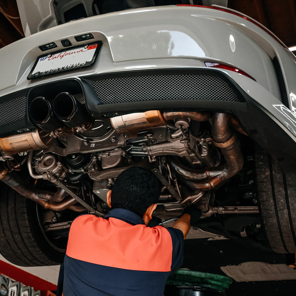 Technician inspecting exhaust and undercar components during maintenance service