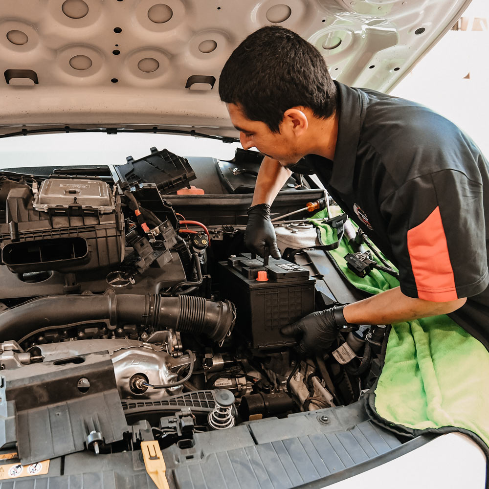 European auto technician installing battery in luxury vehicle during electrical repair service in Los Angeles