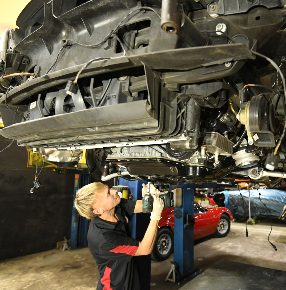 Technician performing transmission and drivetrain repair under vehicle lift