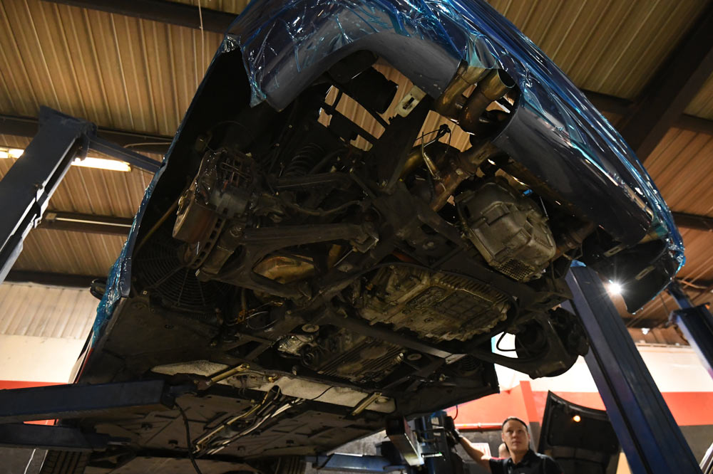 Underside view of Ferrari F355 with engine removed, technician inspecting empty engine bay at European Auto Service Reseda CA