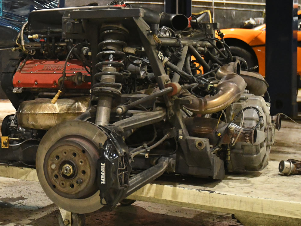 Ferrari F355 engine and transaxle removed as complete assembly with rear suspension — Ferrari-branded brake caliper and red cam covers visible, European Auto Service Reseda Los Angeles