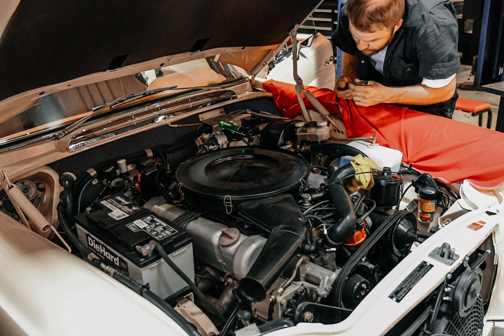 Mechanic inspecting Mercedes 280SE V8 engine bay during diagnostic process