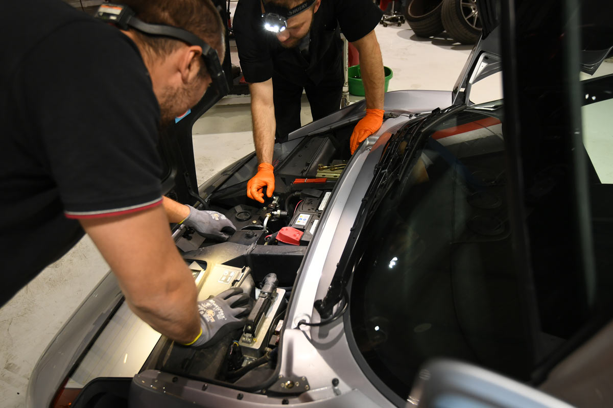European Auto Service technicians inspecting Bugatti EB110 SS front compartment with loupe headlamp in Reseda